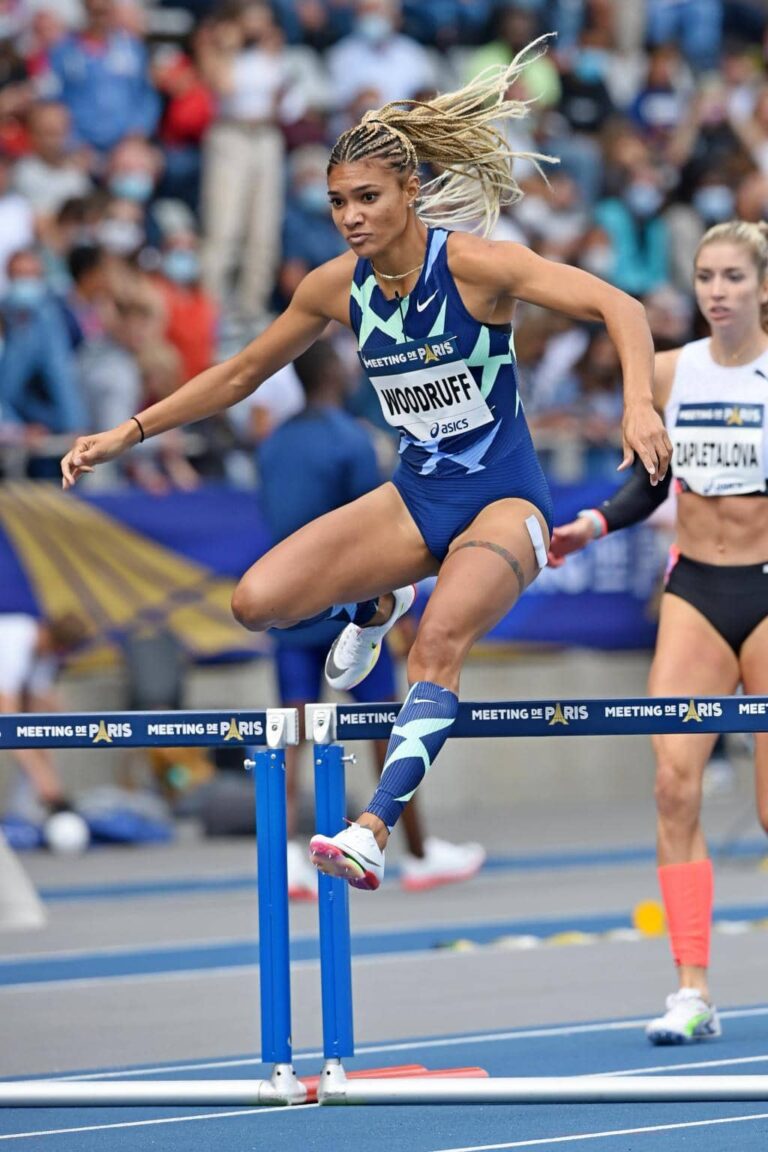 Female track athlete competing in a hurdles race during an international meet, showcasing strength, focus, and athletic excellence featured by HSI.net.